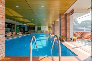 Una piscina interior con agua azul cristalina, rodeada de paredes de ladrillo y plantas en macetas.
