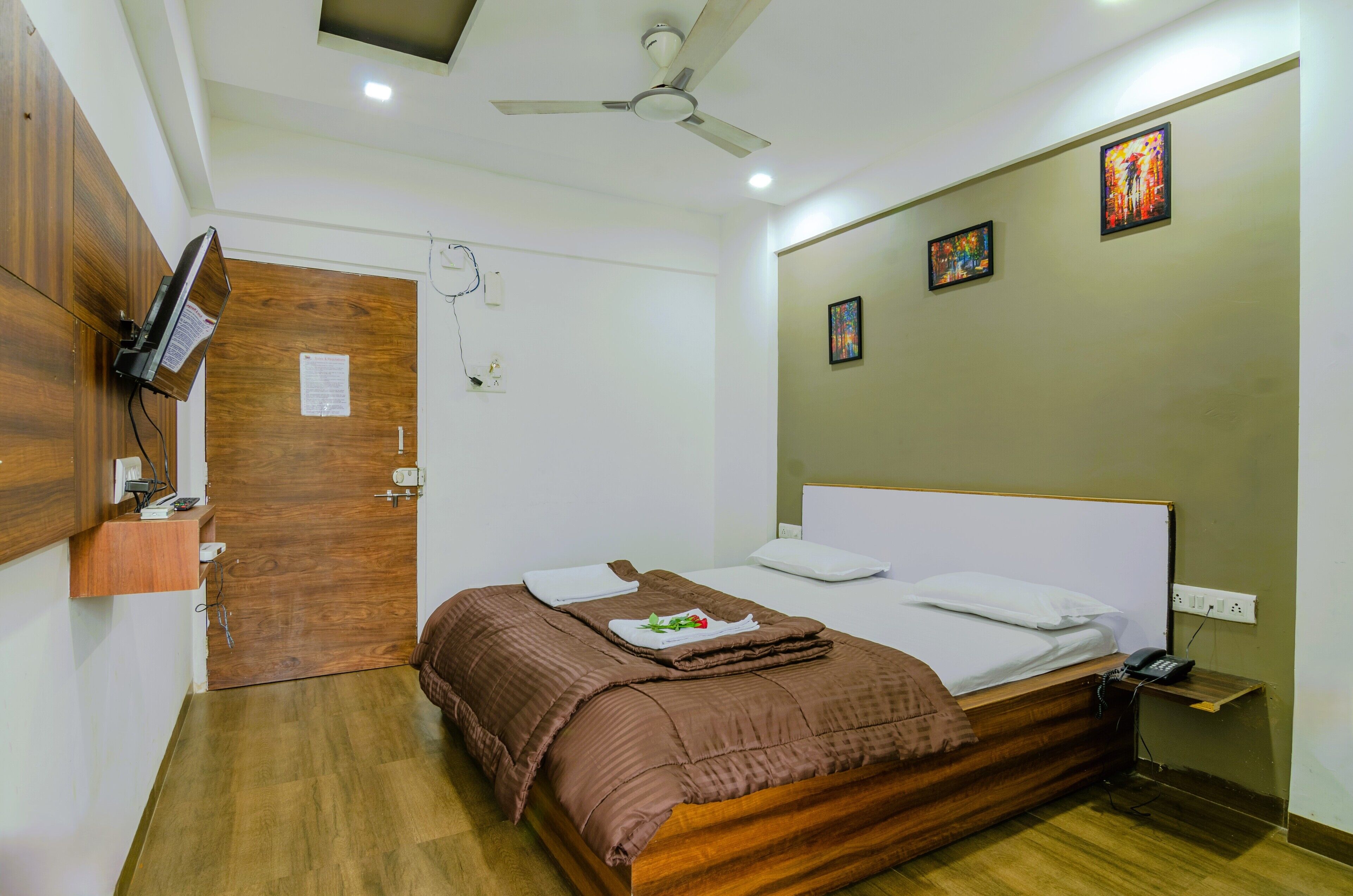 Un dormitorio con una cama de madera, ventilador de techo, televisor montado en la pared y cuadros decorativos.