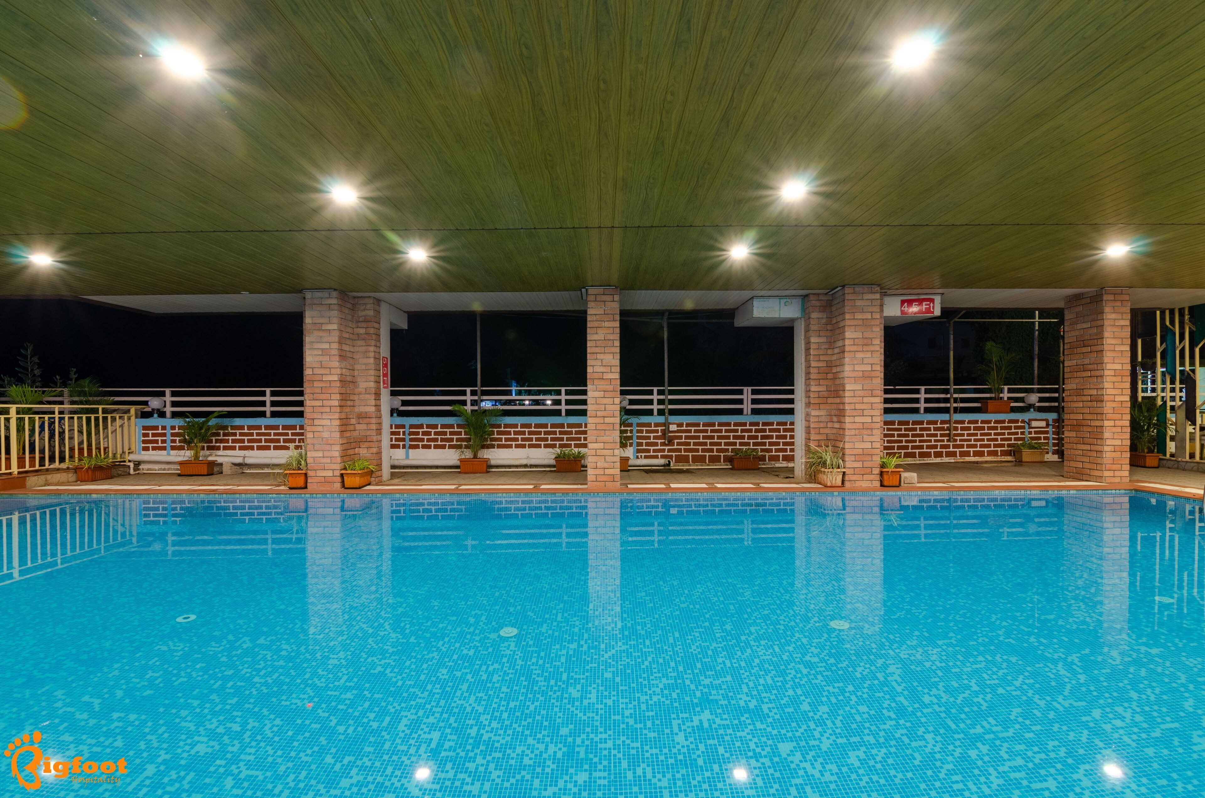 An indoor swimming pool with clear blue water, surrounded by brick pillars and potted plants.