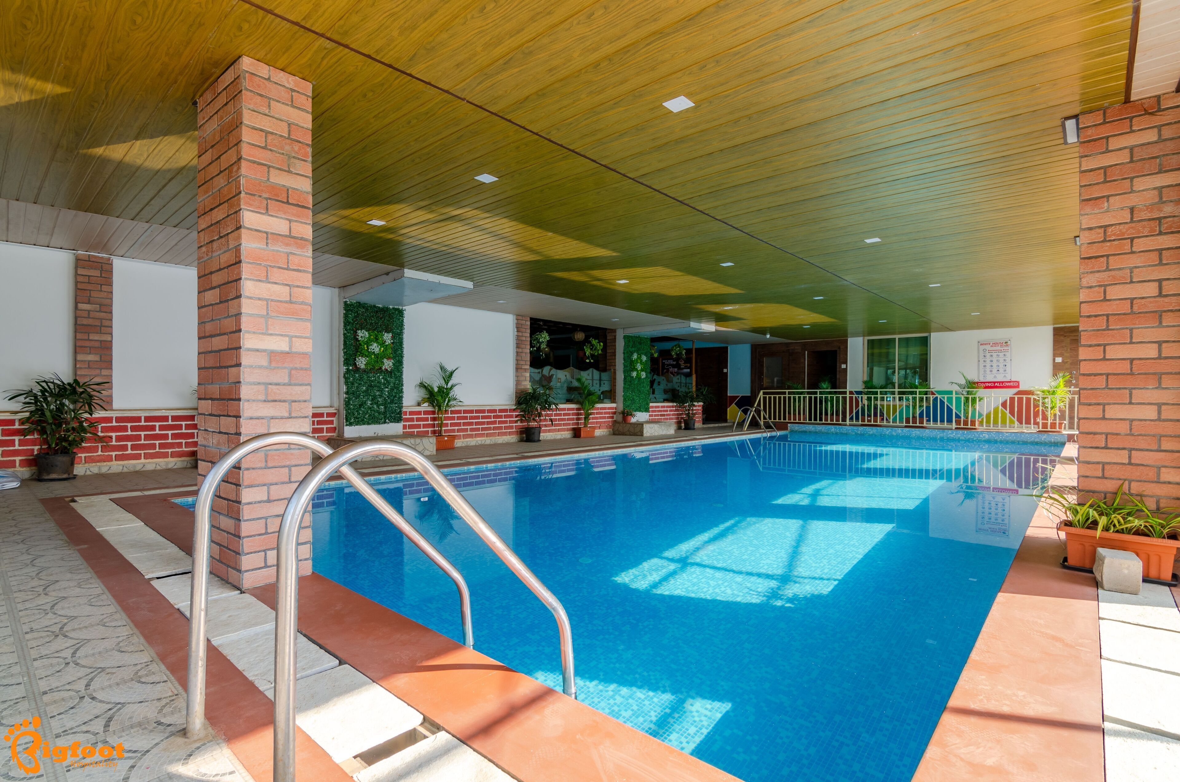 An indoor swimming pool with a clear view of the pool area, surrounded by brick pillars and potted plants.