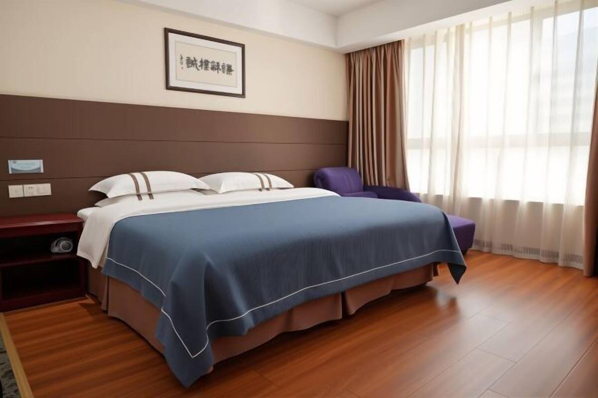 Una habitación de hotel con una cama grande, una mesita de noche, una silla y un ventanal con cortinas.