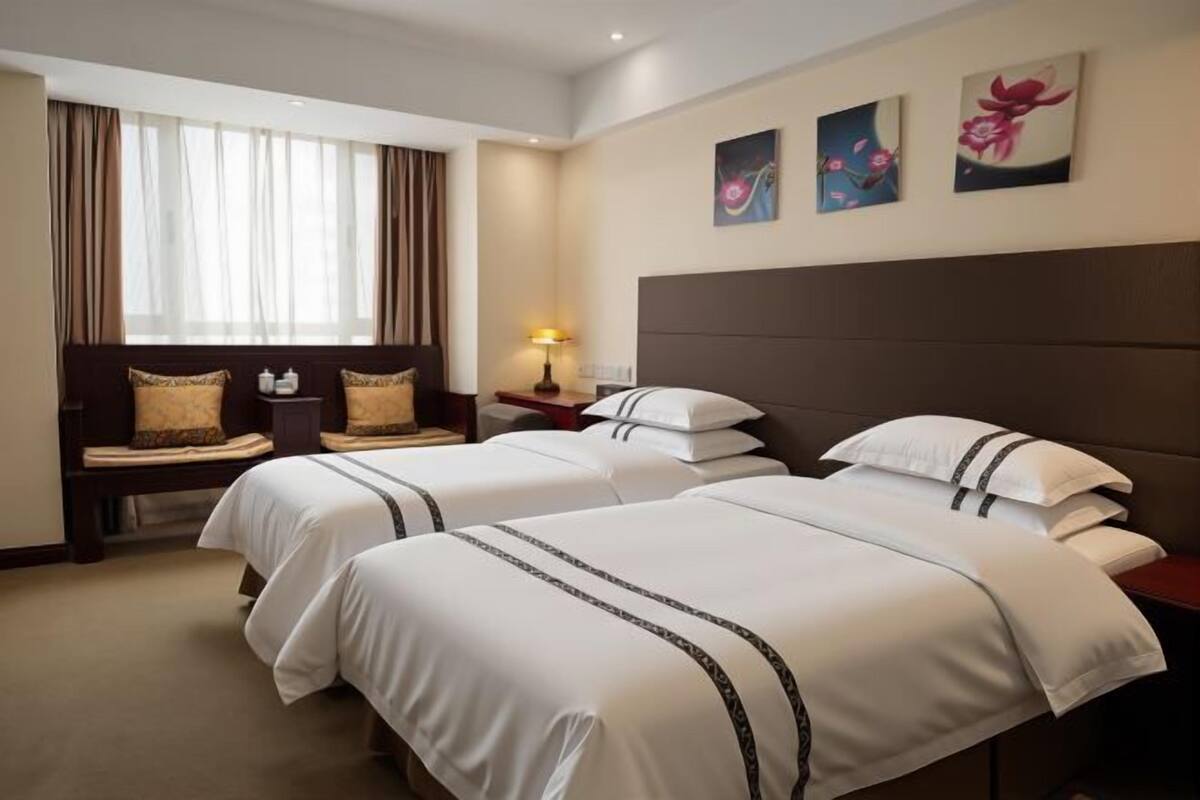 Habitación de hotel con dos camas, una mesita de noche, una lámpara y una ventana con cortinas.