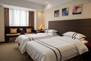 Ein Hotelzimmer mit zwei Betten, einem Nachttisch, einer Lampe und einem Fenster mit Vorhängen.