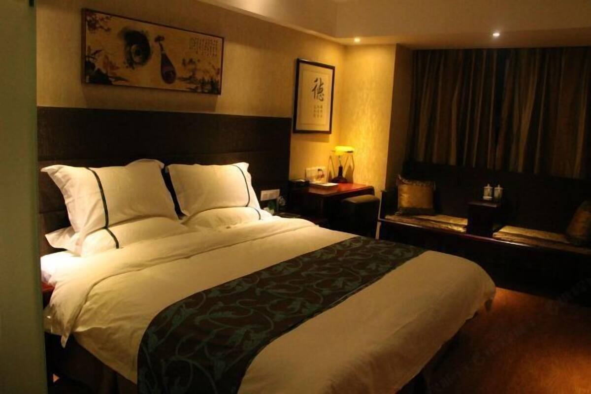 Una habitación de hotel con una cama grande, una mesita de noche con lámpara, una obra de arte enmarcada en la pared y una cortina en la ventana.