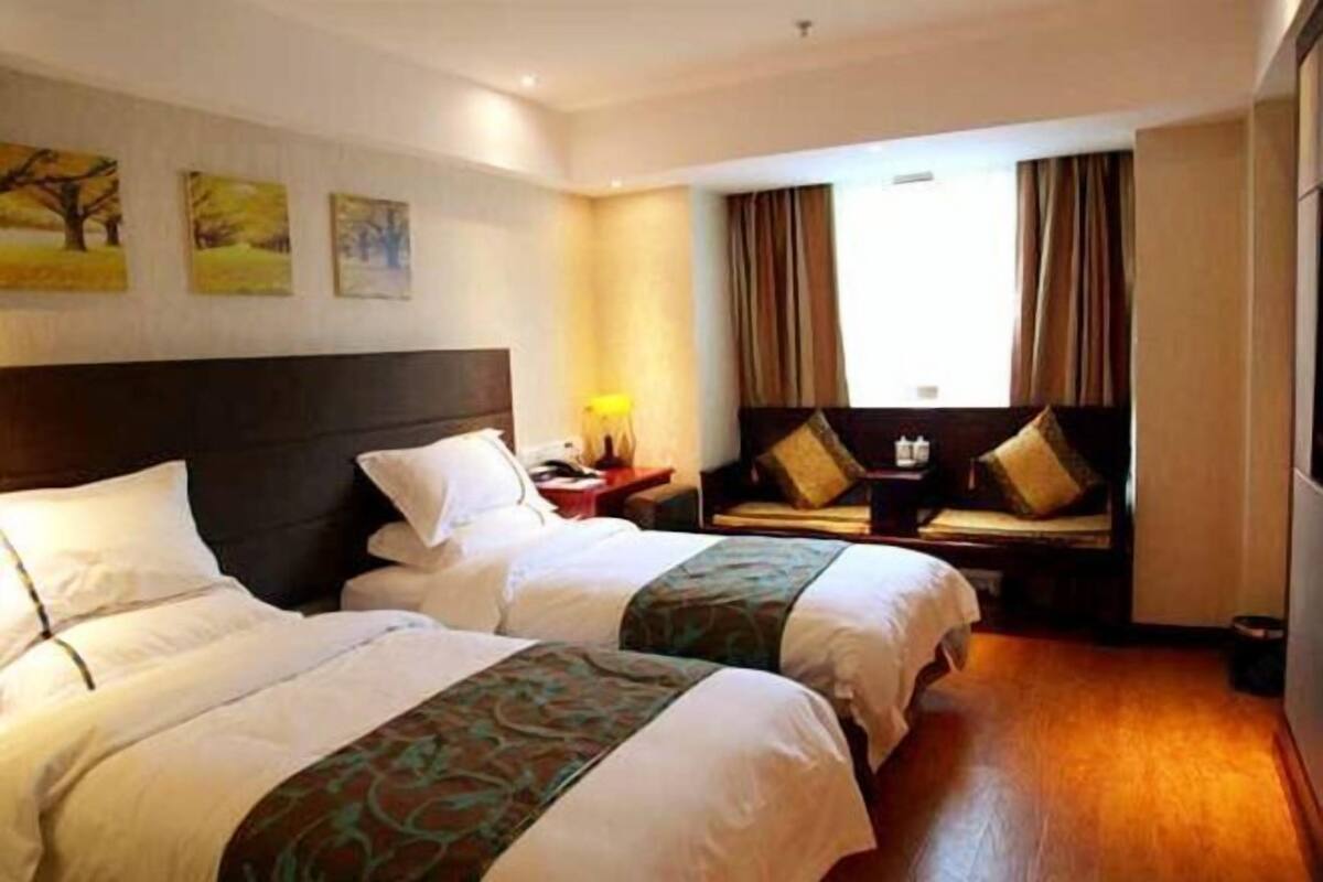 Habitación de hotel con dos camas, una mesita de noche, una lámpara y una ventana con cortinas.