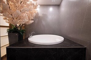 A modern bathroom with a round white sink, dark marble countertop, and a large potted plant with white flowers. - Aurelian Haven Hotel (Hangzhou)