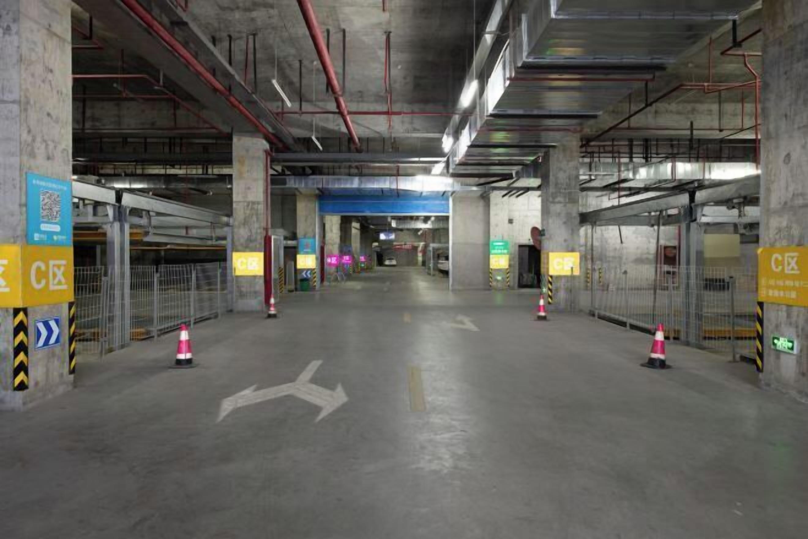An underground parking garage with concrete pillars, directional arrows on the floor, and yellow signage with Chinese characters.