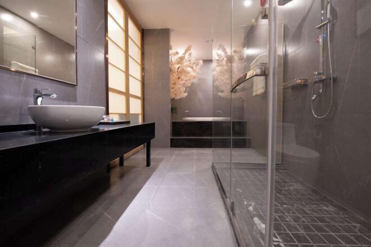 A modern bathroom with a large mirror, a vessel sink, a glass-enclosed shower, and a decorative plant.