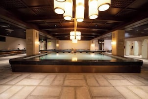 Una amplia piscina interior con un diseño moderno, rodeada de piso de baldosas y vigas de madera en el techo.