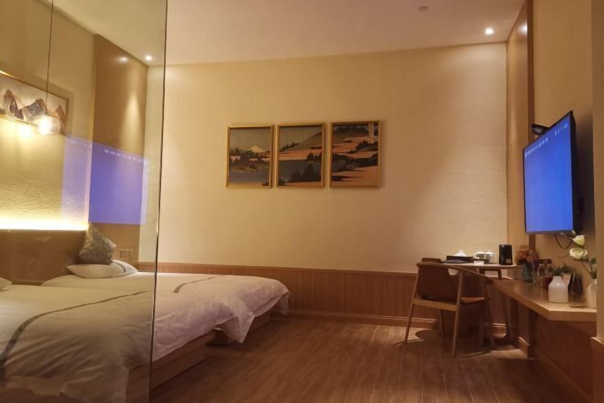 A hotel room with a bed, a desk, and a television. There are three paintings on the wall.