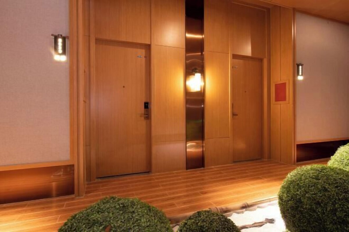 A wooden hallway with a wooden floor, a central elevator, and a small red sign on the wall.
