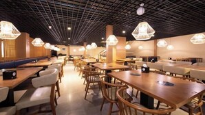 Ein modernes Restaurant mit Holztischen und -stühlen, sechseckigen Pendelleuchten und einer rasterförmigen Decke.