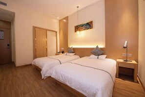 A hotel room with two beds, a wooden floor, a door, a nightstand with a lamp, and a wall-mounted artwork. - Aurelian Haven Hotel (Hangzhou)