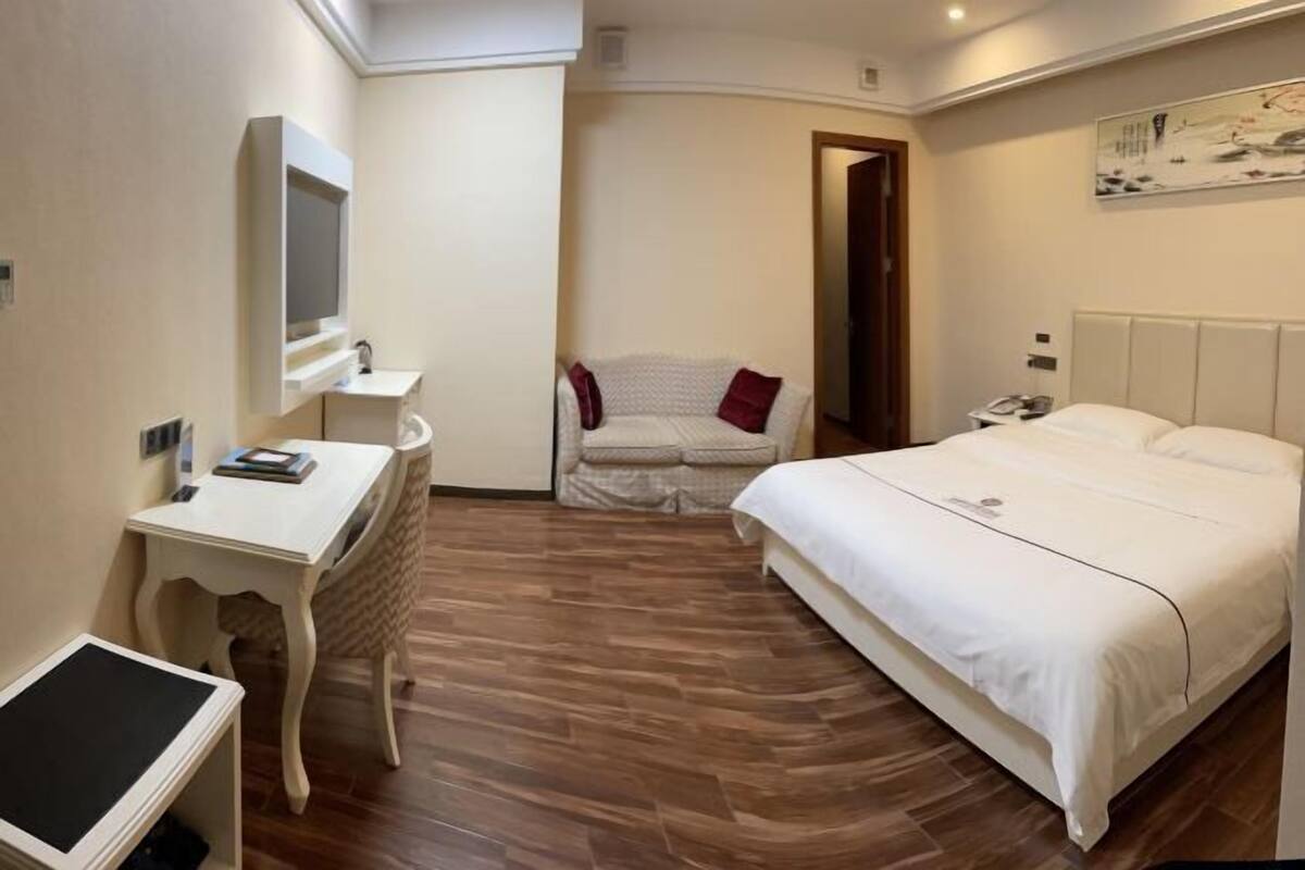 A bedroom with a bed, a desk, a chair, a TV, and a painting on the wall.