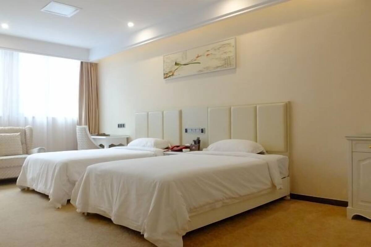 A hotel room with two beds, a sofa, a bedside table, a nightstand, and a painting on the wall.