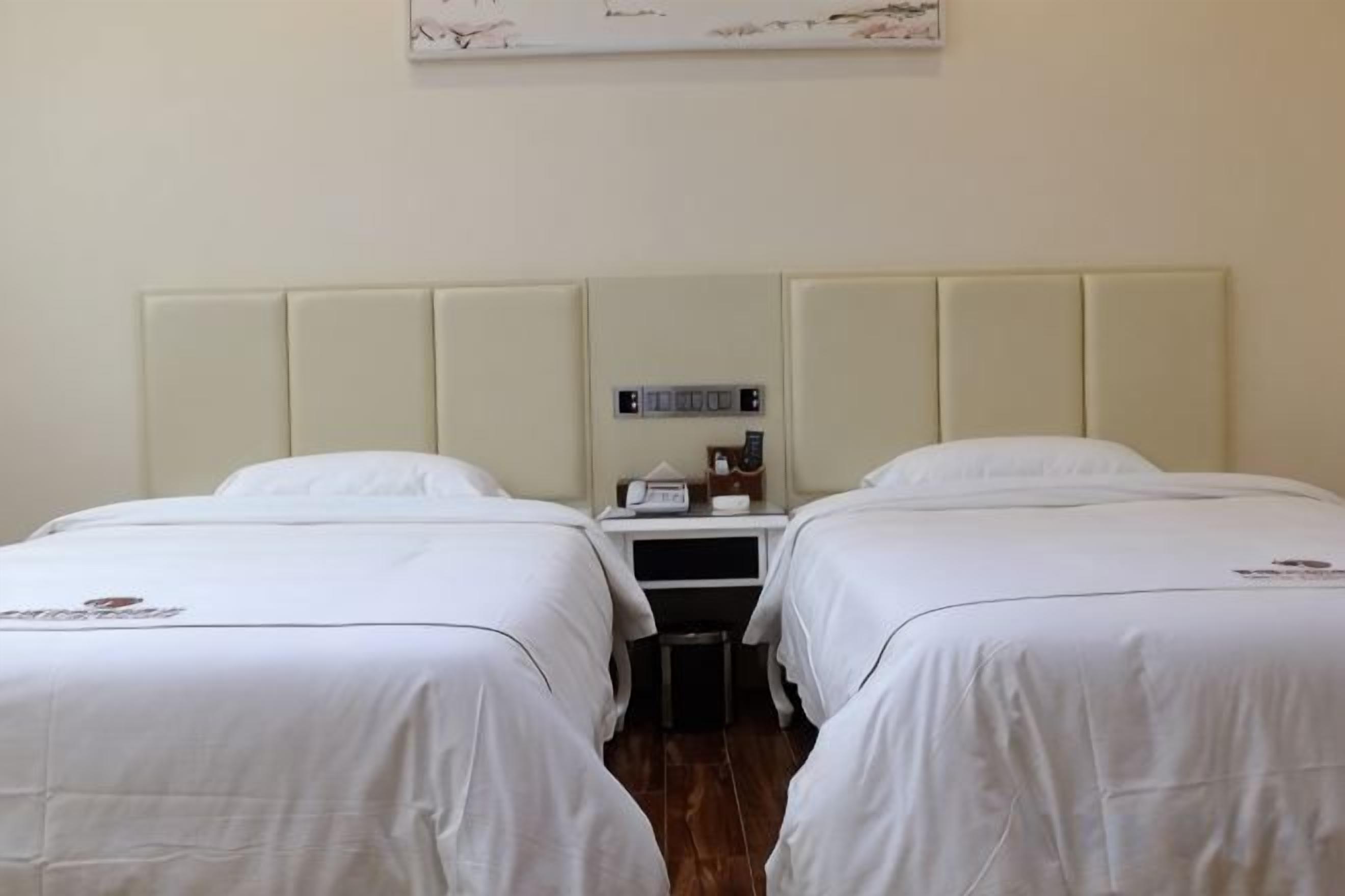 Hotellihuone, jossa on kaksi sänkyä, yöpöytä ja seinälle kiinnitetty kello.