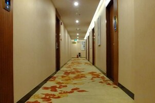 Un pasillo de hotel con pisos alfombrados, puertas a ambos lados y un extintor en la pared derecha.
