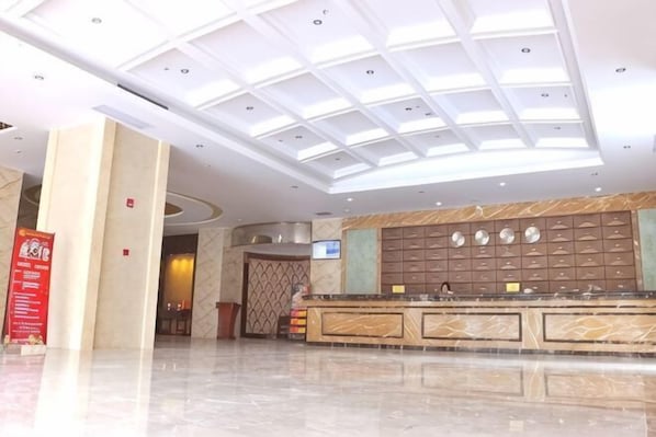 A hotel lobby with a marble reception desk, a large digital screen, and a ceiling with skylights.
