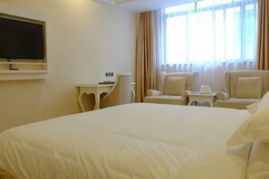 Habitación de hotel con una cama grande, un televisor instalado en la pared, una mesita pequeña y dos sillones.