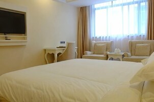 Habitación de hotel con una cama grande, un televisor instalado en la pared, una mesita pequeña y dos sillones.