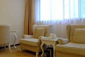 A room with two patterned armchairs, a small white table with a teapot, and a window with curtains.