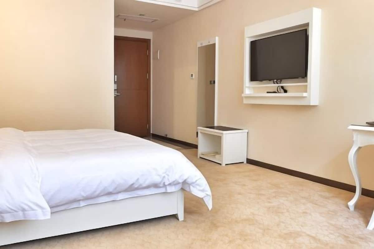 A hotel room with a bed, a TV mounted on the wall, a small table, and a door.