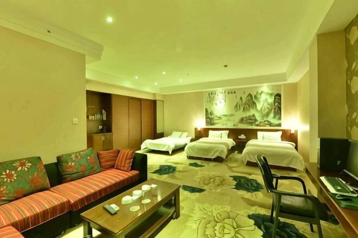 A hotel room with a sofa, two beds, a coffee table, and a TV.