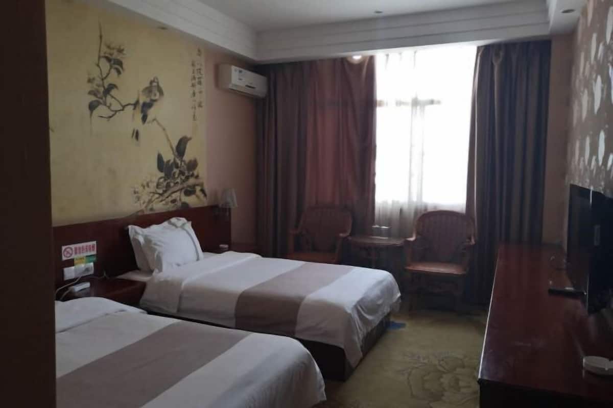 A hotel room with two beds, a television, a desk, and a chair.
