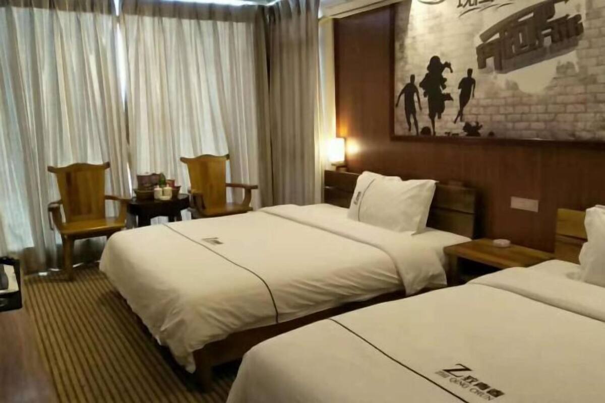 A hotel room with two beds, wooden chairs, a small table, and a wall with a mural.