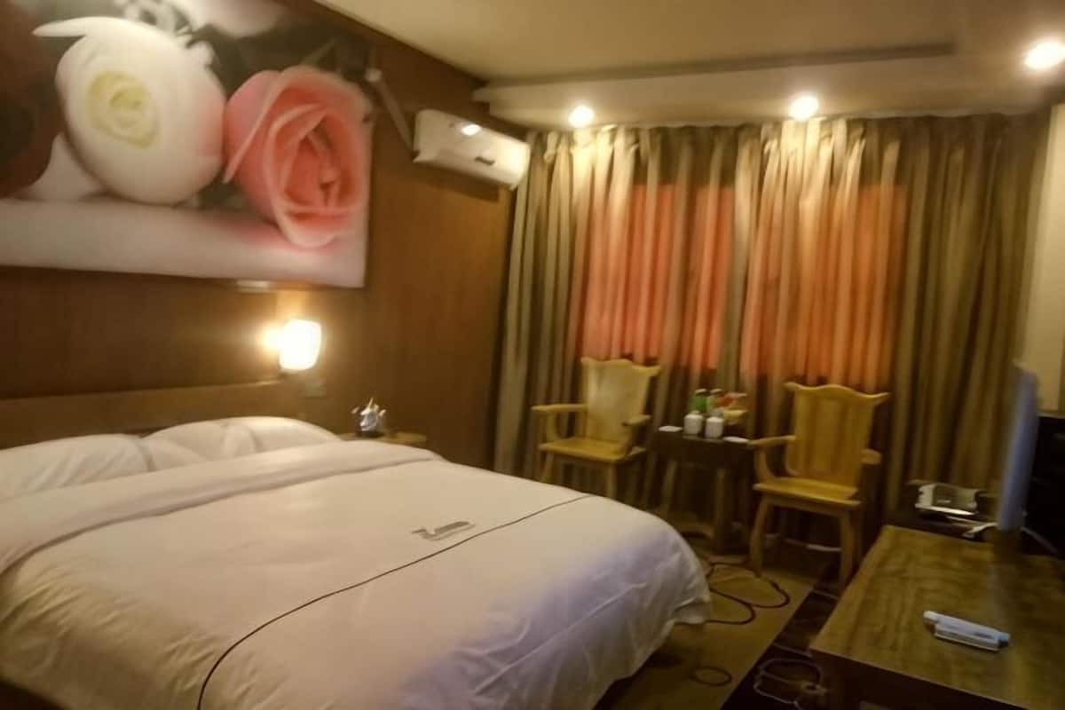 A hotel room with a bed, a desk, two chairs, a television, and a wall-mounted air conditioner.