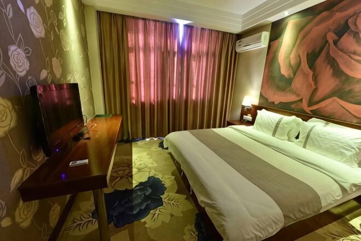 A hotel room with a bed, a desk, a TV, and a painting on the wall.