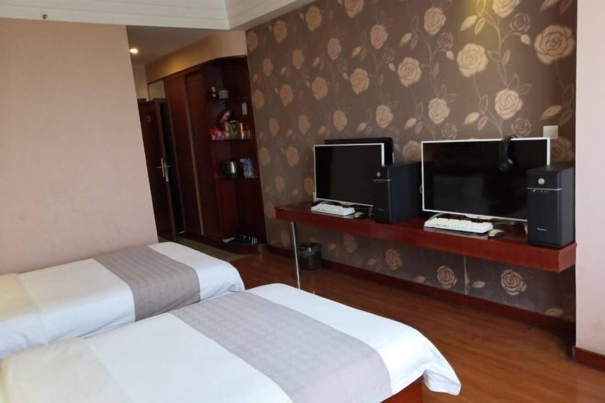 A hotel room with two beds, a TV, a desk with a computer, and a wardrobe.