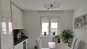 Une cuisine moderne avec des meubles blancs, une table à manger avec des chaises et une fenêtre avec des stores.