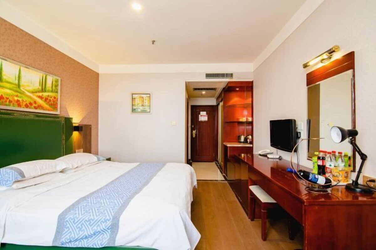 Una habitación de hotel con cama, escritorio, computadora, televisor y espejo.