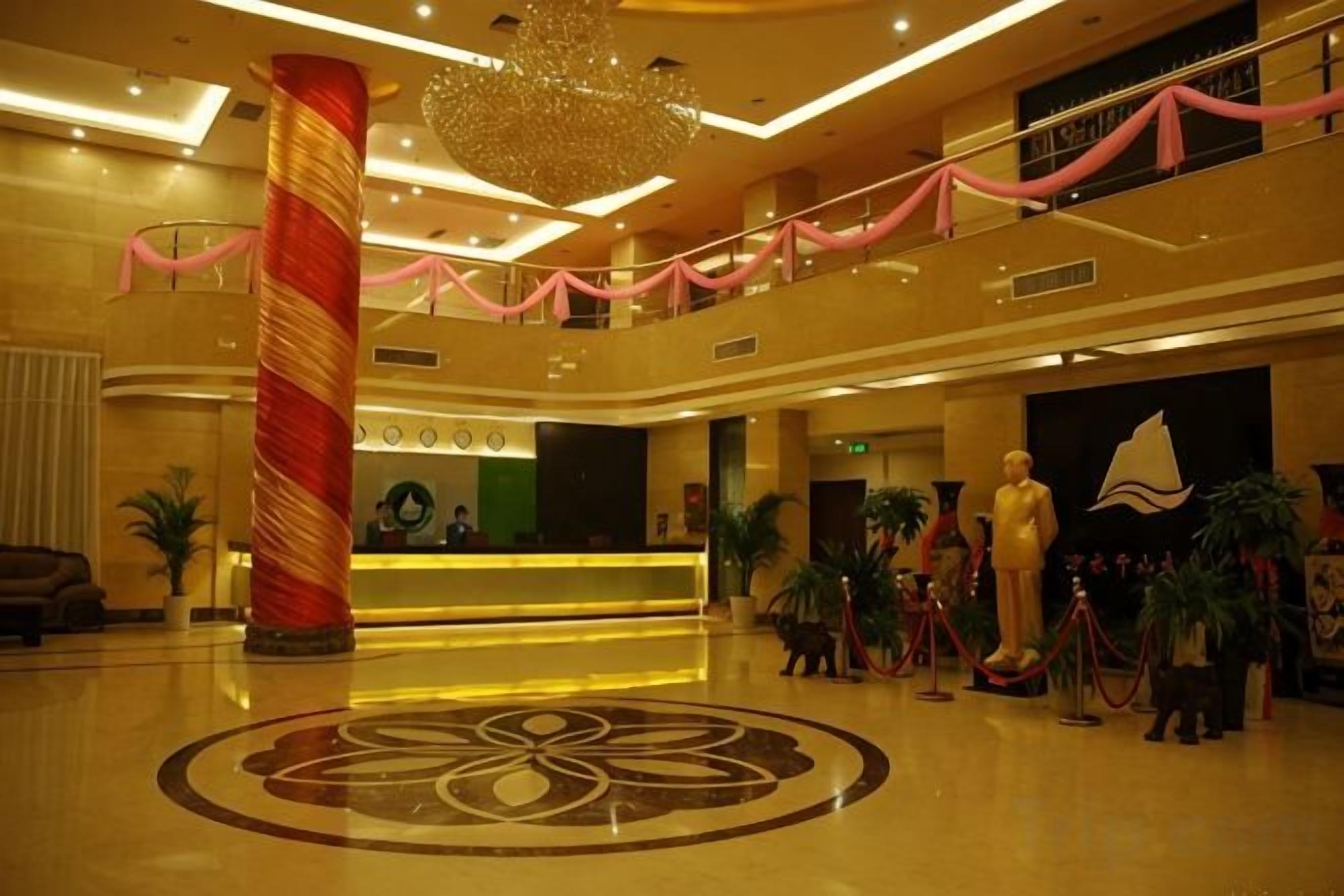 Vestíbulo de hotel con mostrador de recepción, un pilar grande, un diseño decorativo en el suelo y una estatua.