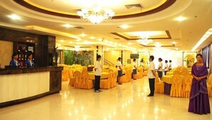 Um saguão de hotel com balcão de recepção, escada e mesas montadas para um evento.