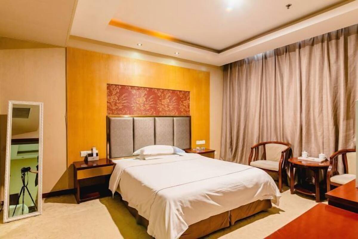 A hotel room with a bed, bedside tables, a mirror, a chair, and a desk.