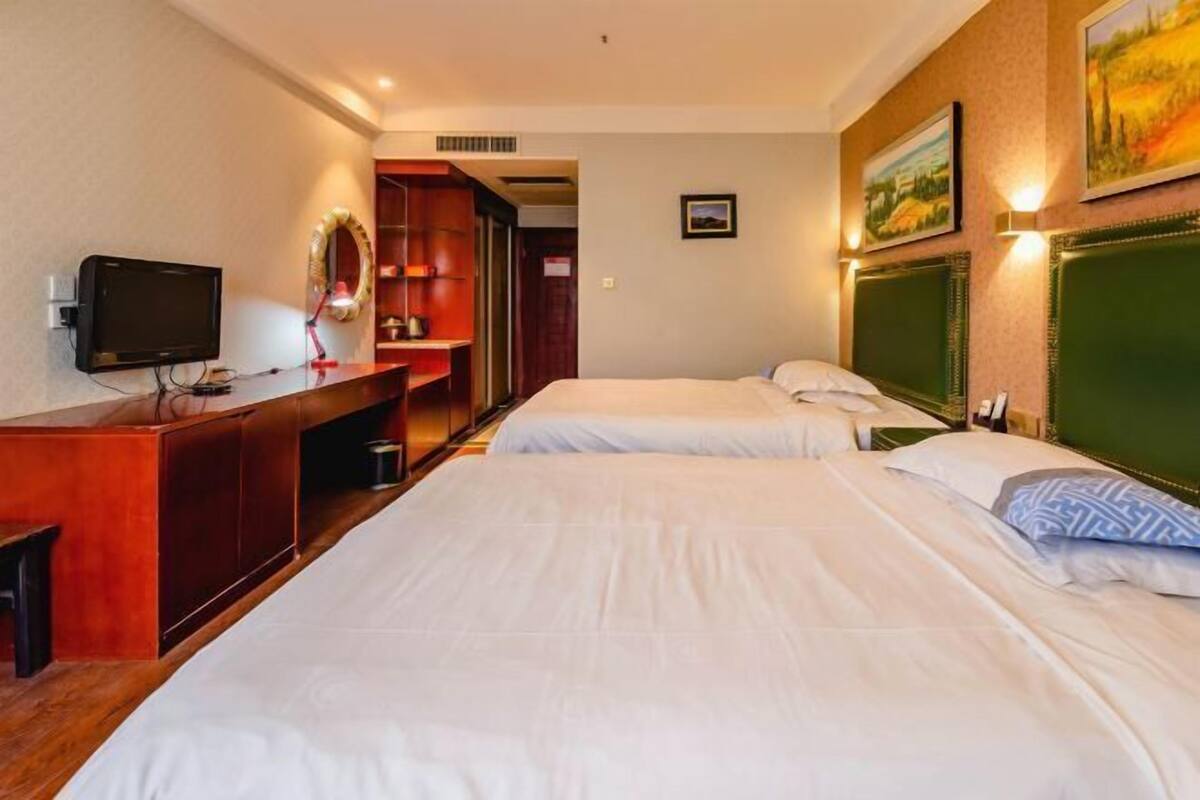 A hotel room with two beds, a desk with a television, and a mirror.