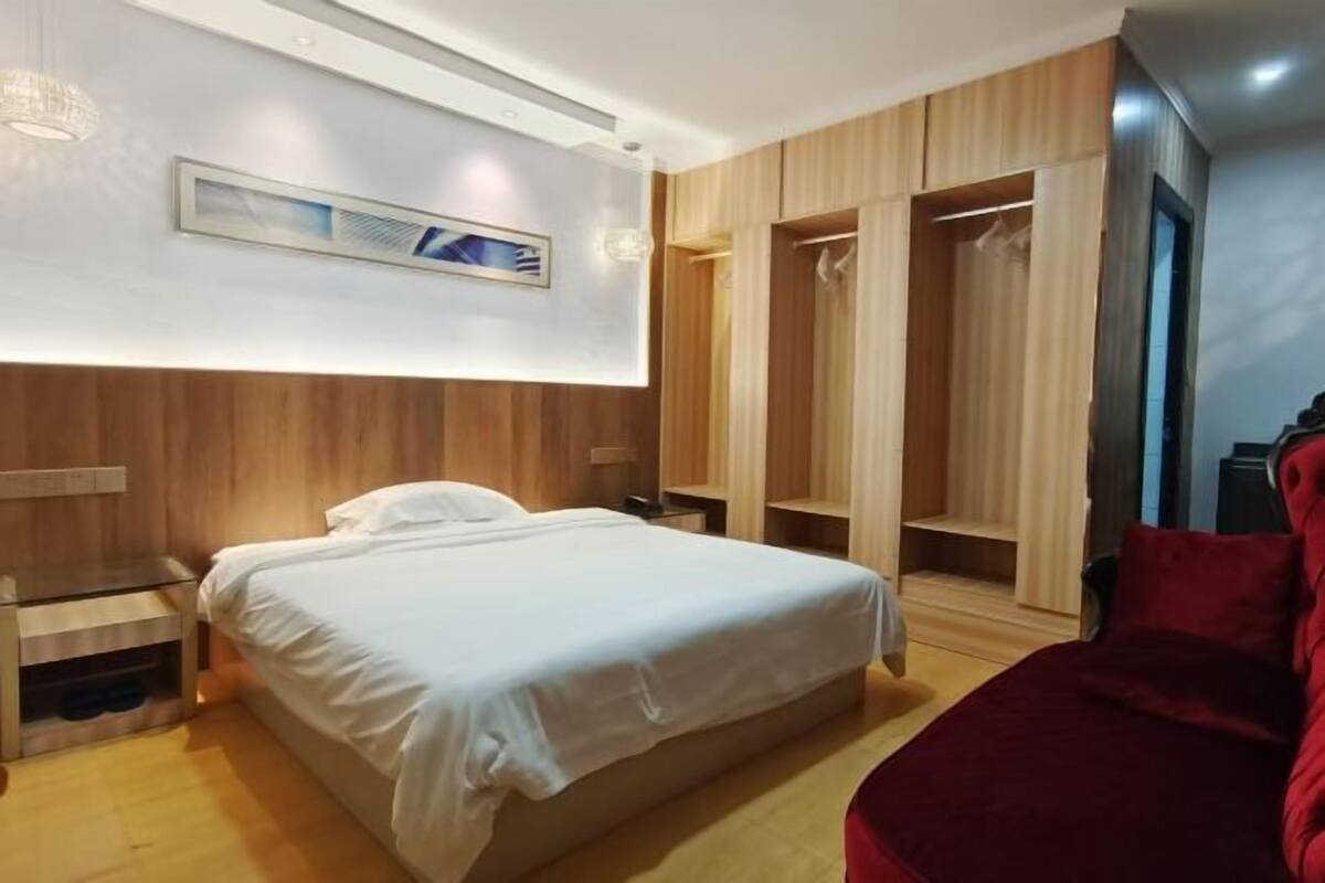 A hotel room with a bed, wooden wardrobe, and a red chair.