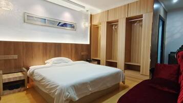A hotel room with a bed, wooden wardrobe, and a red chair.