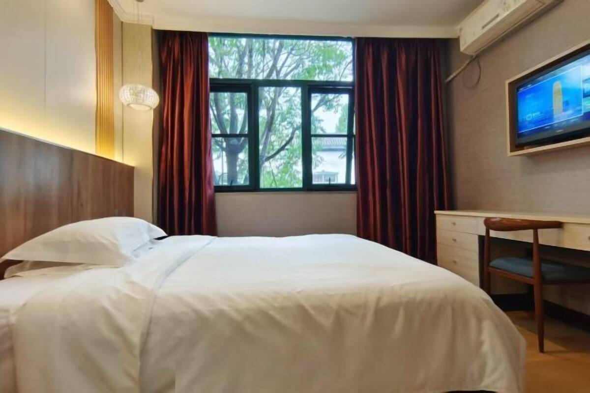 A hotel room with a bed, a desk, a chair, a television, and a window with curtains.