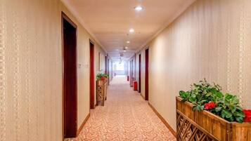 A hotel corridor with patterned carpet, wooden doors, and potted plants.
