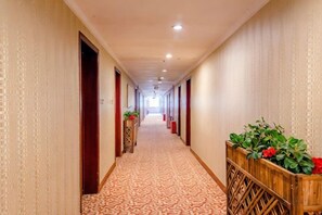 A hotel corridor with patterned carpet, wooden doors, and potted plants. - Wanshui Qianshan Hotel (Xiuwu)