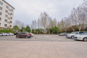A parking lot with several cars, a building with multiple floors, and leafless trees.