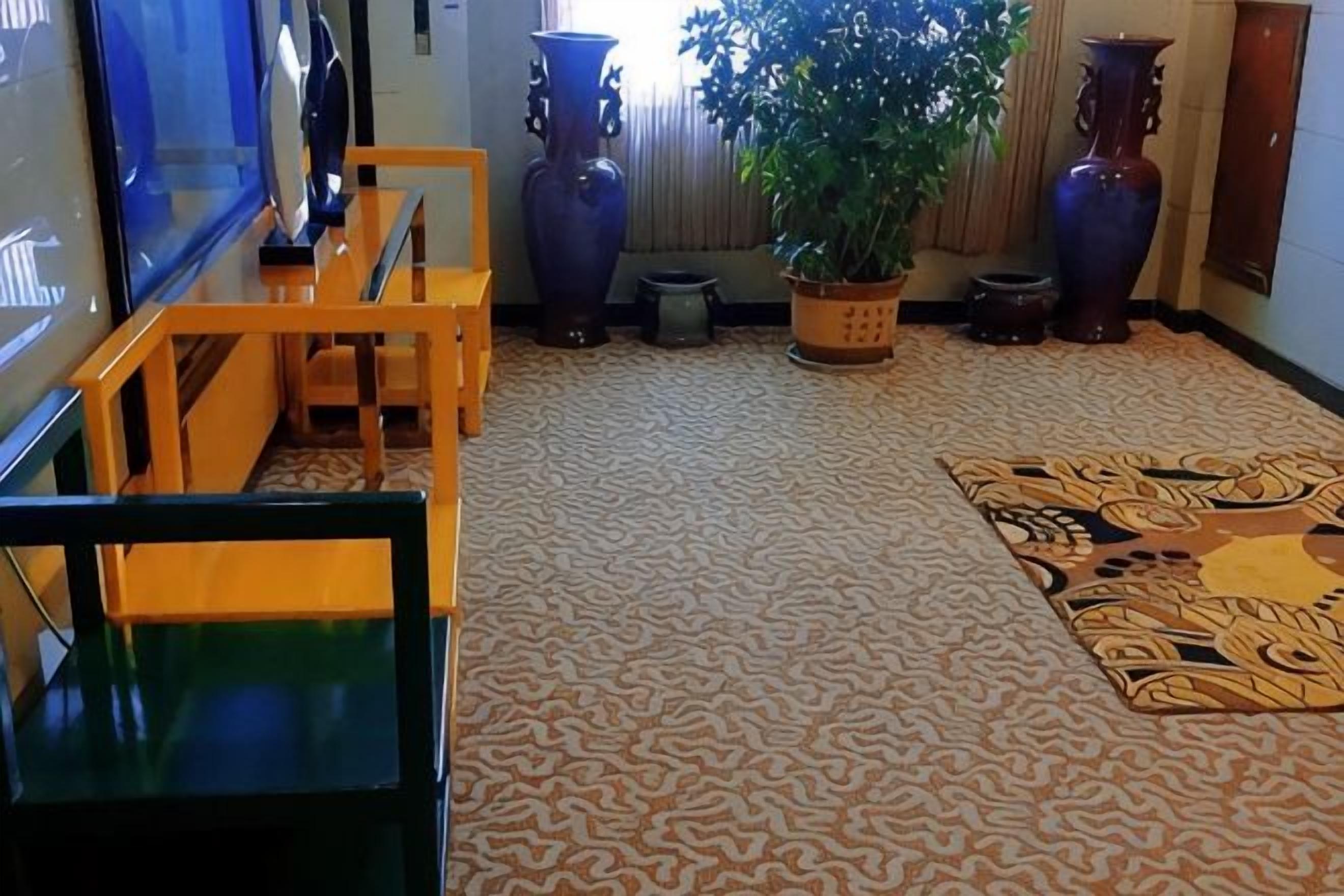 A room with patterned carpet, a wooden bench, a potted plant, and two vases.