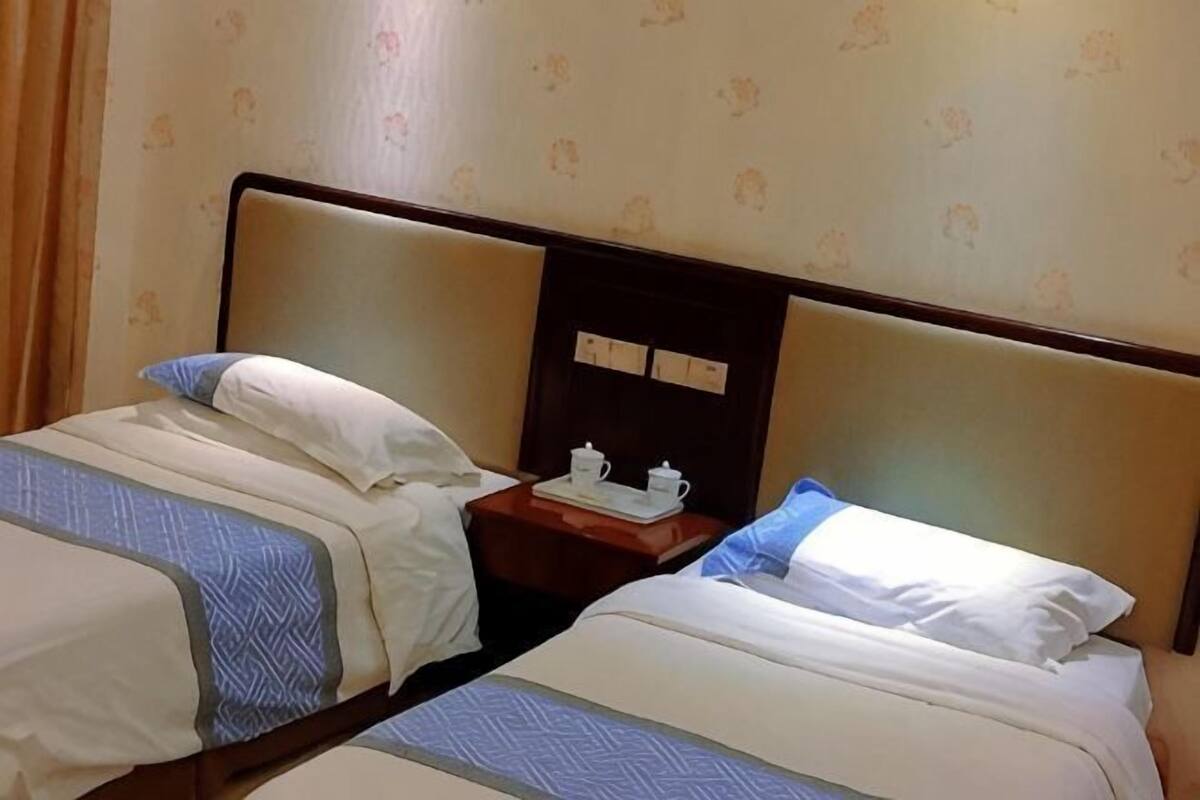Two single beds with headboards, a nightstand with a clock and a cup, and a wall with floral wallpaper.