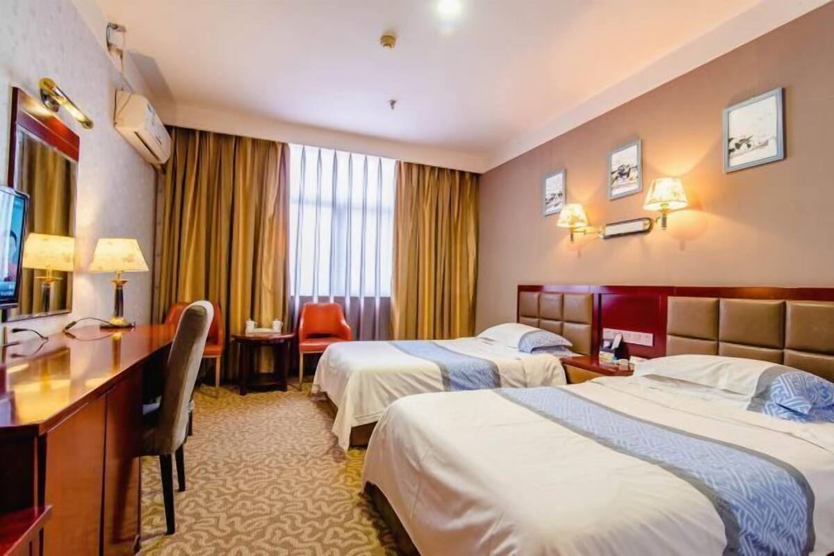 A hotel room with two beds, a desk, a chair, a TV, and a window with curtains.