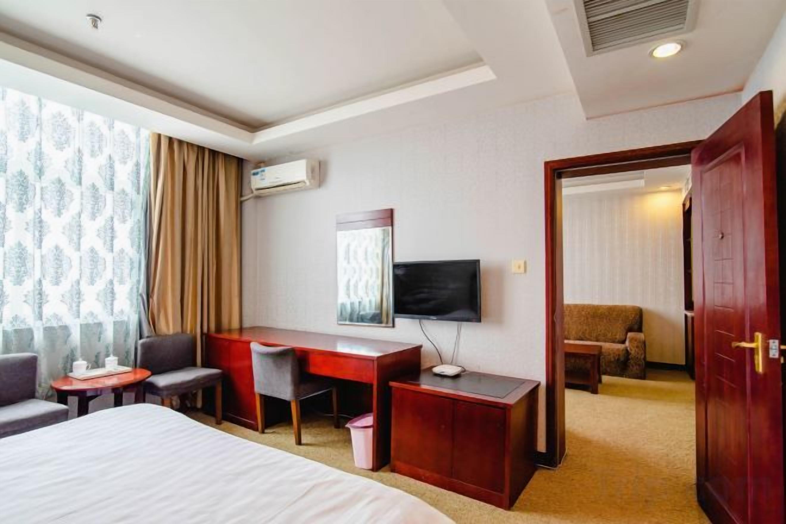 Habitación de hotel con cama, escritorio, silla, televisión y puerta que da a otra habitación.
