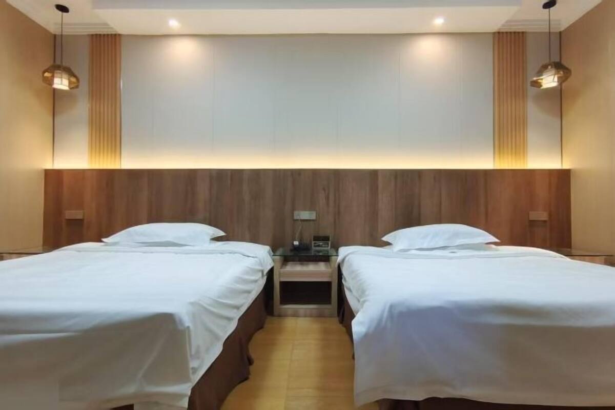 A hotel room with two single beds, a wooden headboard, and a nightstand with a lamp.