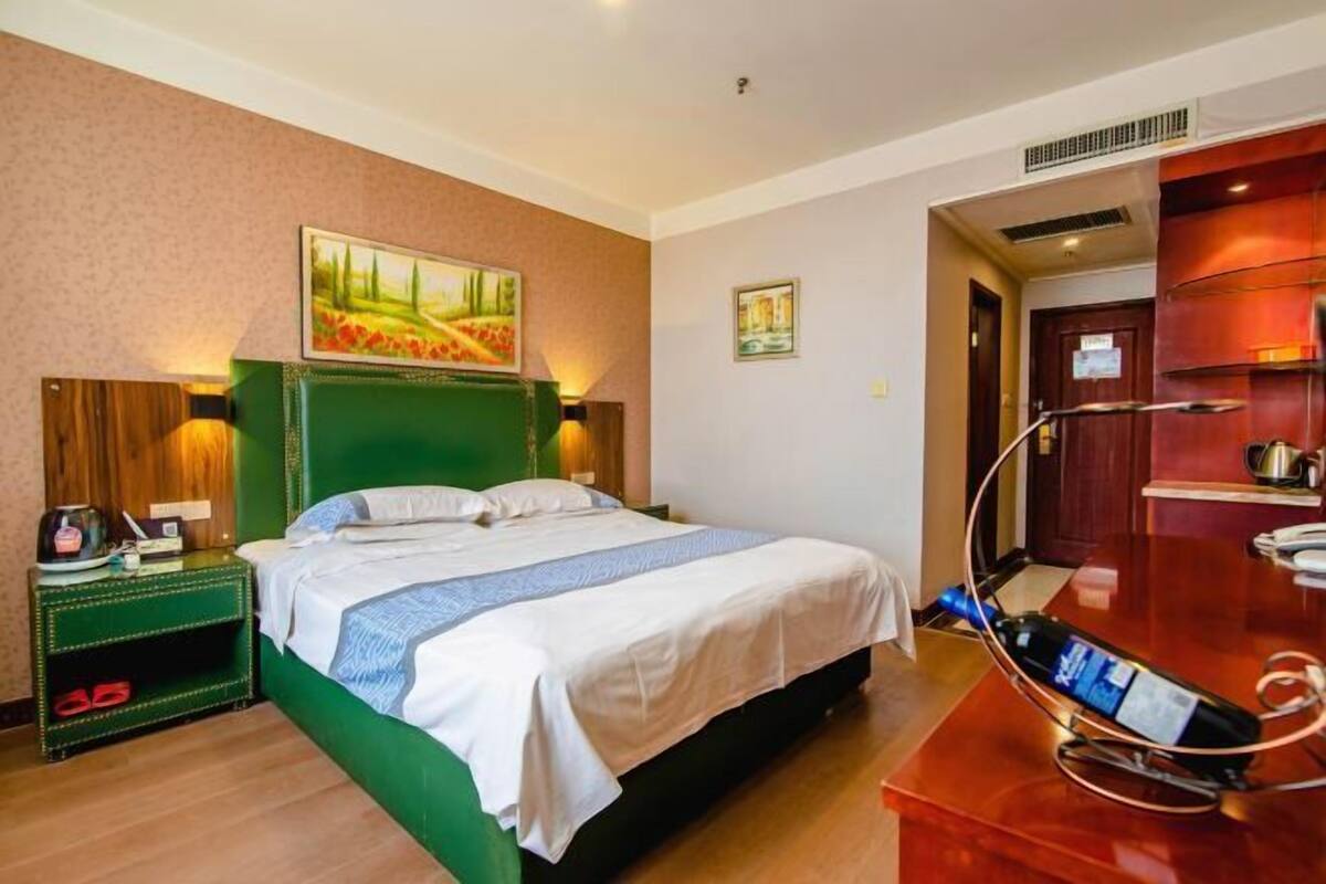 A hotel room with a bed, a nightstand, a desk with a laptop, and a painting on the wall.